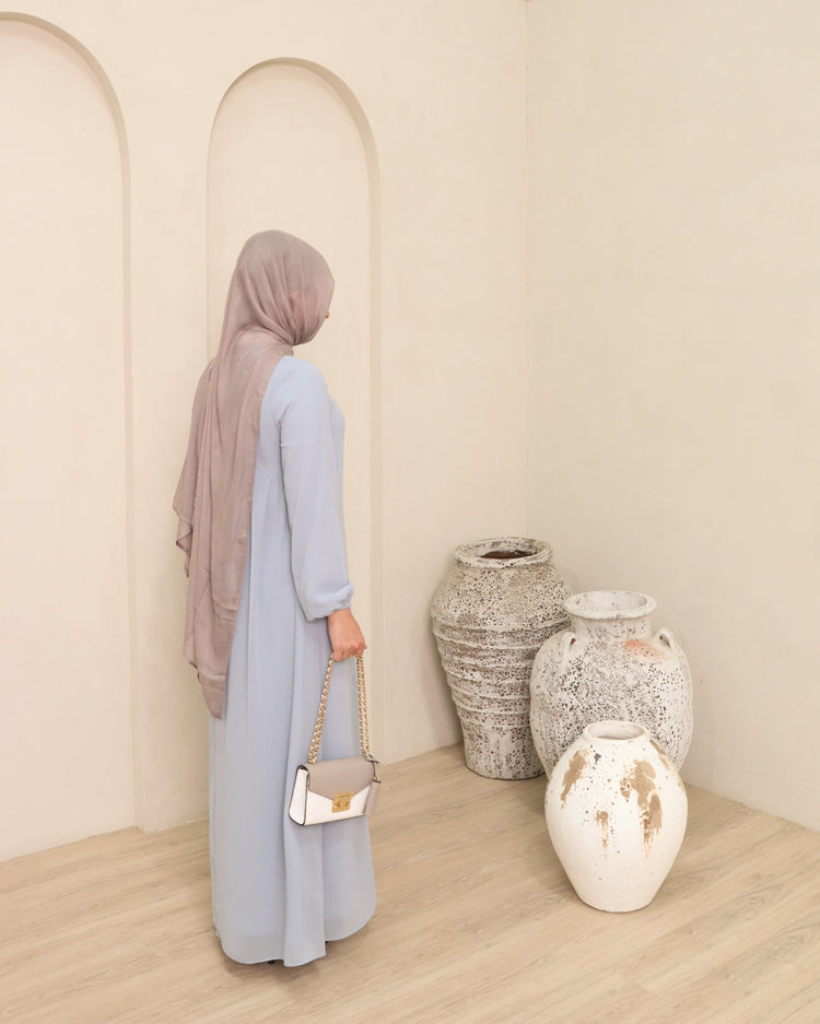 Woman in a light blue maxi dress standing beside white arches and stone vases