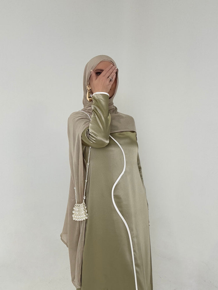 Woman in an olive satin dress with a wavy white trim and a pearl bag